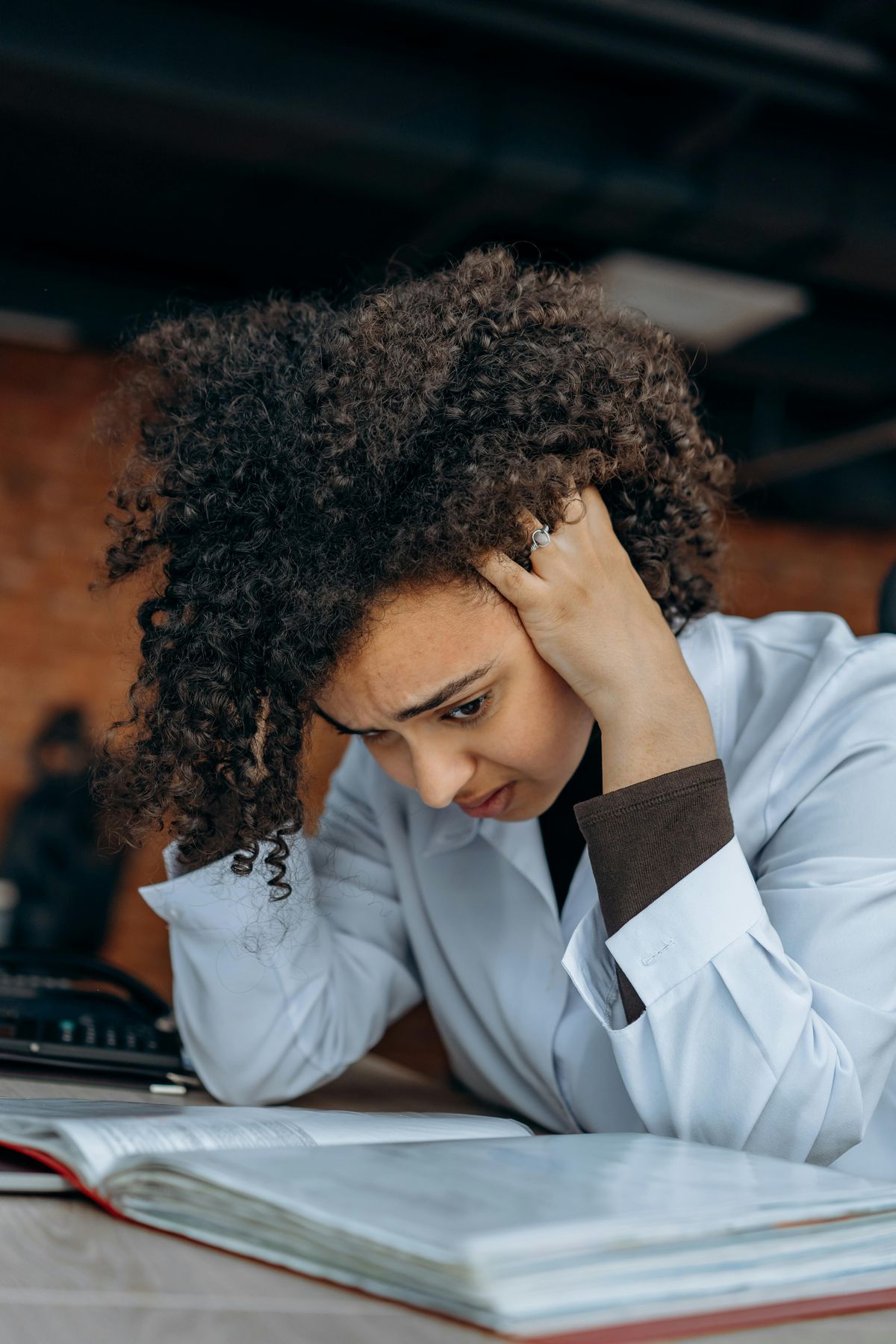 A woman at a desk with her hand against her head, overwhelmed by papers and a binder